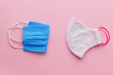 Yeniden kullanılabilir yüz maskesi ve pembe arka planda tek kullanımlık tıbbi maske. Coronavirüs salgını sırasında sıfır atık kavramı. Tek kullanımlık maske ve el yapımı tekstil maskesi