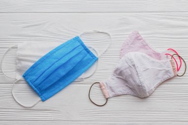Yeniden kullanılabilir yüz maskeleri ve beyaz ahşap arka planda tek kullanımlık tıbbi maskeler. Virüs salgını sırasında sıfır atık yaşam tarzı. Tek kullanımlık maske ve el yapımı tekstil maskesi