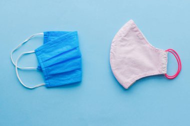 Tekrar kullanılabilir yüz maskesi ve mavi arka planda tek kullanımlık tıbbi maske. Virüs salgını sırasında sıfır atık yaşam tarzı. Tek kullanımlık maske ve el yapımı tekstil maskesi