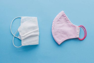 Virüs salgını sırasında sıfır atık yaşam tarzı. Tekrar kullanılabilir yüz maskesi ve mavi arka planda tek kullanımlık tıbbi maske. Tek kullanımlık maske ve el yapımı tekstil maskesi