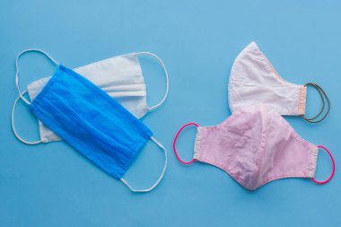 Yeniden kullanılabilir yüz maskeleri ve mavi arka planda tek kullanımlık tıbbi maskeler. Virüs salgını sırasında sıfır atık yaşam tarzı. Tek kullanımlık maske ve el yapımı tekstil maskesi