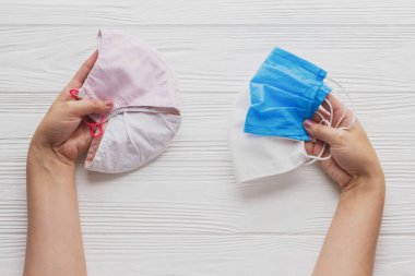 Yeniden kullanılabilir yüz maskeleri seçin. Eller tekrar kullanılabilir ve tek kullanımlık tıbbi maskeleri beyaz ahşap arka planda tutuyor. Koronavirüs karantinasında sıfır atık. Tek kullanımlık ve el yapımı tekstil maskesi