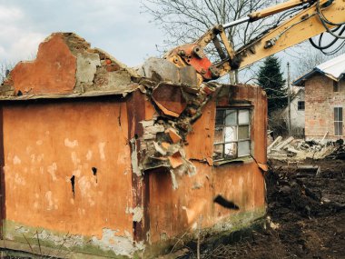 Kazıcı kırsaldaki tuğla evi yok ediyor. Buldozer eski tuğlalardan toprak ve çöplerle dolu duvarlardan beton topluyor. Kazma makineleri evi mahvediyor