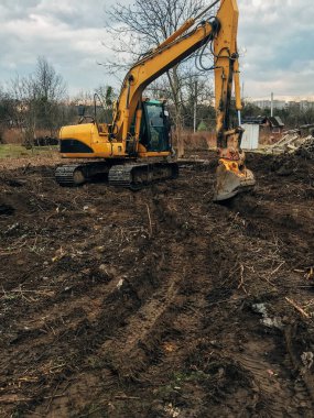 Kazıcı, kırsaldaki ağaçların kökünü kazıyor. Buldozer eski ağaçları, kökleri ve dalları toprak ve çöplerle temizliyor. Kazma makineleri. Bahçe işleri