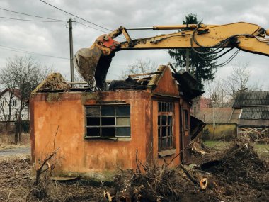 Kazıcı kırsaldaki tuğla evi yok ediyor. Buldozer eski tuğlalardan toprak ve çöplerle dolu duvarlardan beton topluyor. Kazma makineleri evi mahvediyor