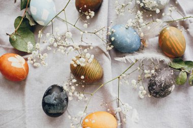 Kırsal masa üzerindeki paskalya yumurtaları düzleşmişti. Doğal renklerle boyanmış paskalya yumurtaları bahar beyaz çiçekleri ve kırsal tekstil arka planında tüyler. Mutlu Paskalyalar.