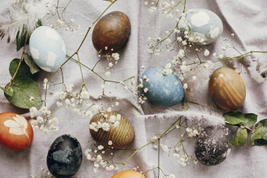 Kırsal masa üzerindeki paskalya yumurtaları düzleşmişti. Doğal renklerle boyanmış paskalya yumurtaları bahar beyaz çiçekleri ve kırsal tekstil arka planında tüyler. Mutlu Paskalyalar.