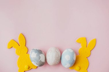 Şık paskalya yumurtaları, pembe kağıt masanın üstünde sarı tavşan düz yatak, mesaj için yer. Doğal boyanmış paskalya yumurtaları ve tavşan süslemeleri. Kart modeli. Mutlu Paskalyalar.