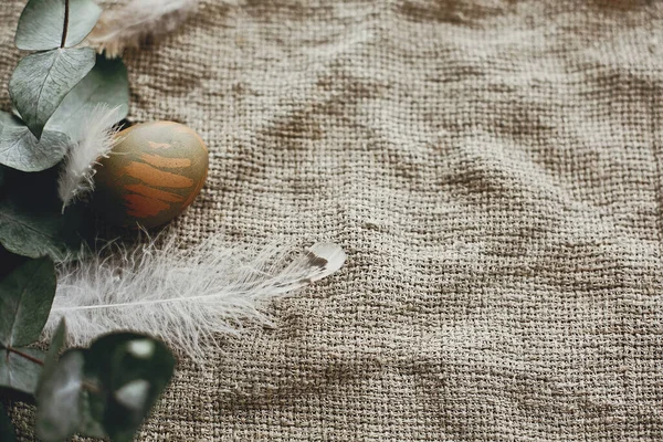 带羽毛的乡村鸟巢中的美味的复活节蛋放在乡村餐桌上 在农村纺织品背景上涂有桉树枝条的天然绿色彩蛋 平躺在床上案文的篇幅 — 图库照片