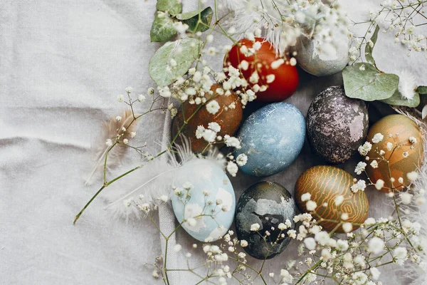 在平铺的桌子上的乡村鸟巢中 有一些美味的复活节蛋 天然色彩艳丽的彩蛋 春白色的花朵和羽毛在农村纺织品背景上 复活节快乐 — 图库照片