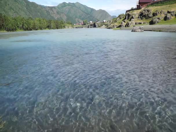 Быстрый поток воды в горной реке с небольшой деревней в фоновом режиме — стоковое видео