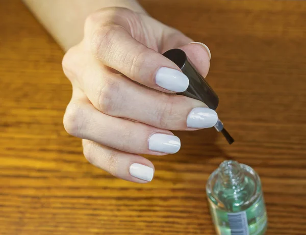 Jednej strony kobieta z białym manicure trzymać pędzel z lakierem bezbarwnym — Zdjęcie stockowe