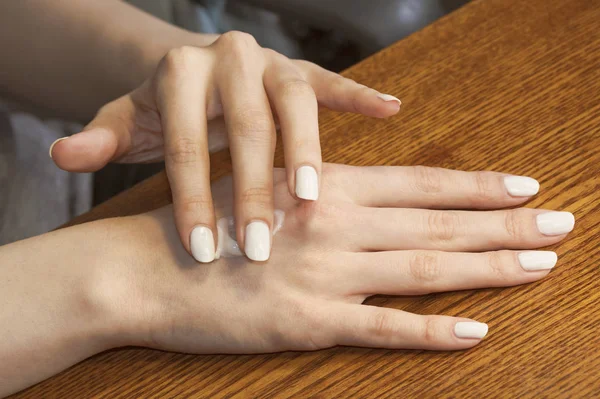 As mãos femininas aplicam o creme na pele — Fotografia de Stock