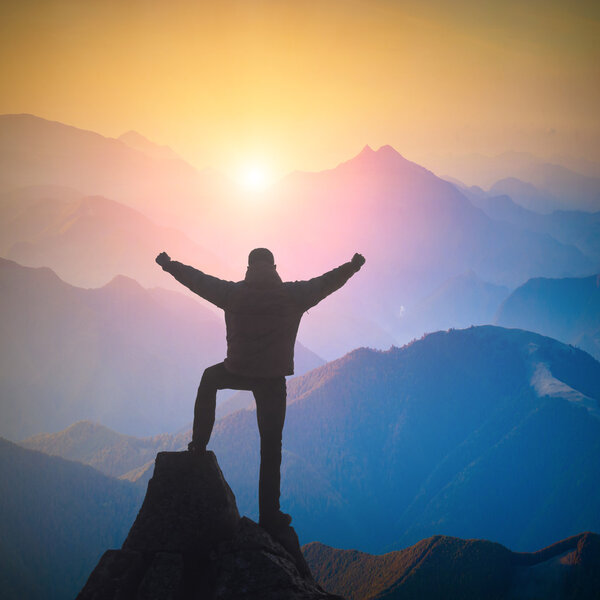 Турист, стоящий на краю скал и радующийся восходу солнца
