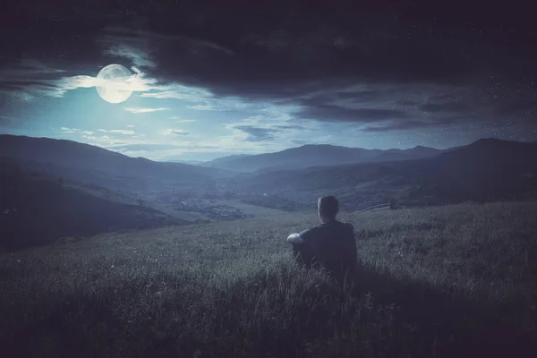 Человек сидит на холме и наслаждается восходом луны. Стиль Instagram — стоковое фото