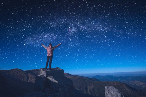 Man standing on a rocky cliff with raised hands — Stock Photo, Image