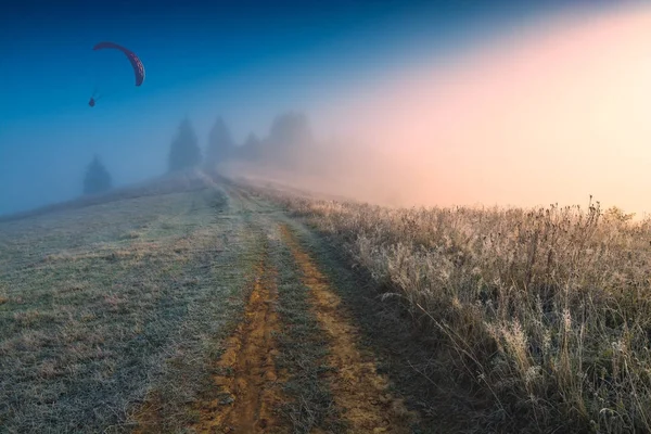 Paplanernyővel silhouette repül át a ködös alpesi völgy — Stock Fotó