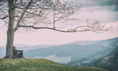 Bir vadide büyük ağacın altında oturan adam