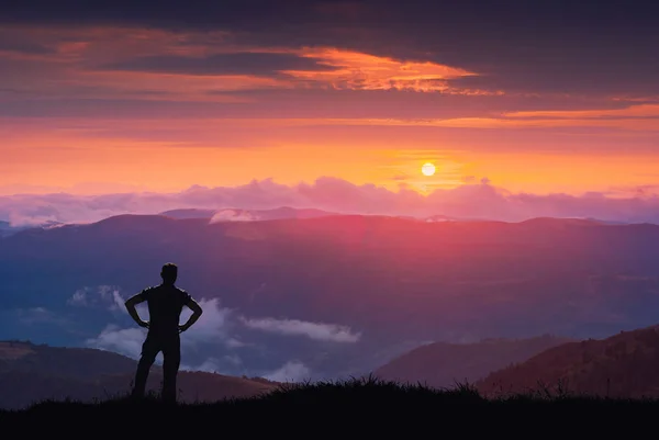 Silueta turista na kopci proti barevné majestátní západ slunce — Stock fotografie