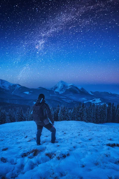 Un excursionista con mochila de pie en una ladera nevada por la noche — Foto de Stock