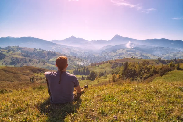 Mladý muž tramp sedí na kopci v zelené trávě — Stock fotografie
