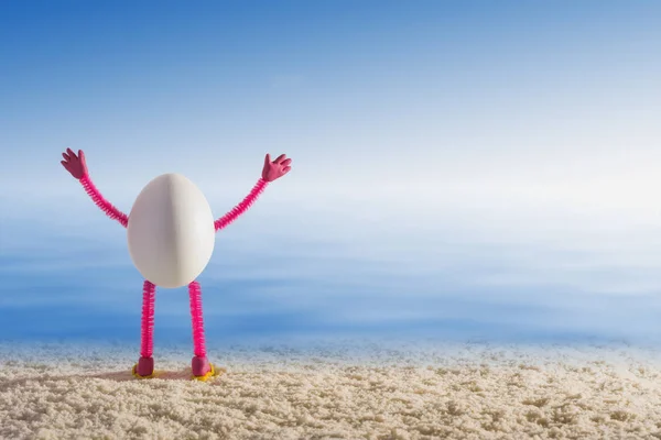 Egg standing on a sandy beach with raised hands — Stock Photo, Image