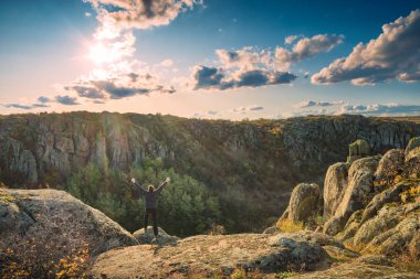 Elleri havada bir adam bir kayanın üzerinde duruyor.