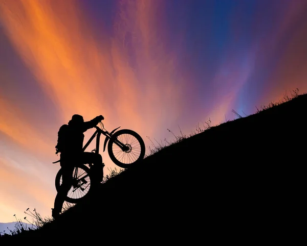 自転車をカラフルな夕日に対して上り坂のプッシュサイクリスト 極端なスポーツとエンデューロバイクの概念 — ストック写真