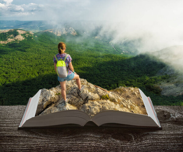 Girl hiker with backpack in a mountain valley on a pages of an open book. Travel concept.