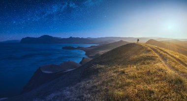 Gündüz ve gece arasında. Deniz kenarındaki bir tepede sırt çantalı bir kız yürüyüşçü. Peri masalı kavramsal manzara.