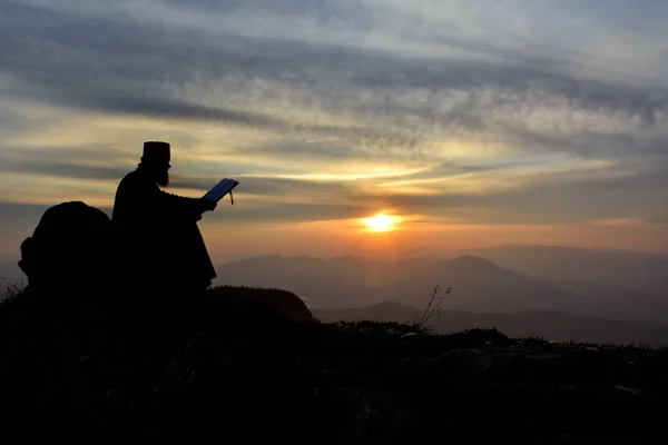 Silhouette del sacerdote che legge alla luce del tramonto, Romania — Foto Stock