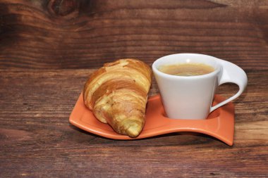 Ahşap masa üzerinde izole bir kruvasan ile kahve fincanı