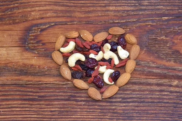 Mixed nuts and dried fruits forming a heart-shape on wood background — Stock Photo, Image