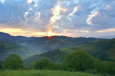 Yeşil otlar ile güzel dağ çayır. Güneş doğuyor. vahşi Transilvanya tepelerde manzara. Holbav. Romanya. 