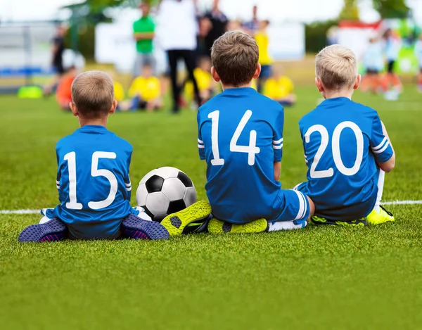 Crianças em Blue Sportswear sentadas no campo de futebol e assistindo futebol jogo de futebol. Torneio de futebol infantil. Antecedentes do futebol juvenil — Fotografia de Stock