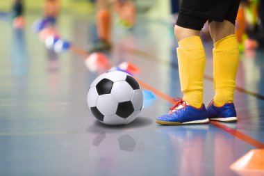 Children training soccer futsal indoor gym. Young boy with soccer ball training indoor football. Little player in yellow sports socks clipart