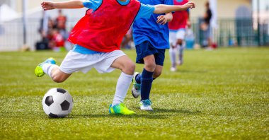 Genç erkek futbol topu tekmeleme yeşil Saha çimen. Futbol Okulu turnuva çocuklar için. Kırmızı ve mavi forma gömlek top için mücadele oyuncular