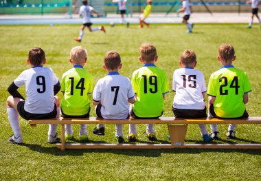 Futbol oynayan çocuklar. Genç futbolcular. Tahta bankta oturan genç futbol takımı. Çocuklar için futbol maçı. Turnuva futbol maçı oynayan genç erkek. Gençlik futbol kulübü futbol takımı oyuncuları