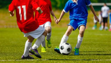 Çocuklar doğal çim sahada futbol spor oynarken. Mavi ve kırmızı futbol forma çimenlerin üzerinde topu tekmeleme çocuklar. Çocuklar için futbol maçı