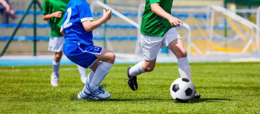 Çocuk futbol oyuncu topu ile çalışan. Sahada futbol oynayan çocuklar içinde mavi ve yeşil futbol formaları. Spor stadyum içinde belgili tanımlık geçmiş