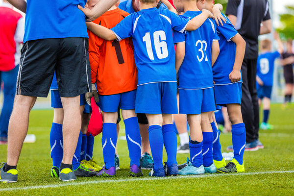 Детская футбольная команда. Дети, стоящие вместе на поле. Тренер молодёжного футбола мотивирует игроков перед матчем
