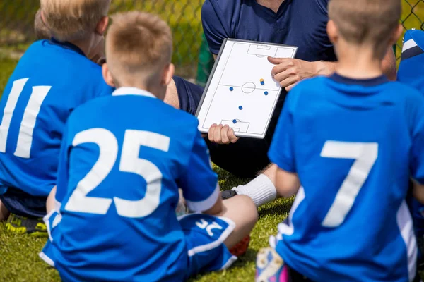 Kinderfußballtrainer. Fußballmannschaft mit Trainer im Stadion. Jungen hören vor dem Wettkampf auf die Anweisungen des Trainers. Trainer hält Mannschaftsvortrag mit Fußball-Taktik-Brett — Stockfoto