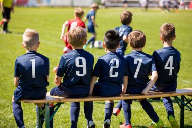 Çocuklar bir bankta oturan takım spor. Çocuklar futbol oyuncu grubu. Çocuk futbol kulübü. Futbol Futbol Turnuvası çocuklar için oyun. Çimenli sahada futbol topu tekmeleme çocuklar. Çocuklar açık havada spor.