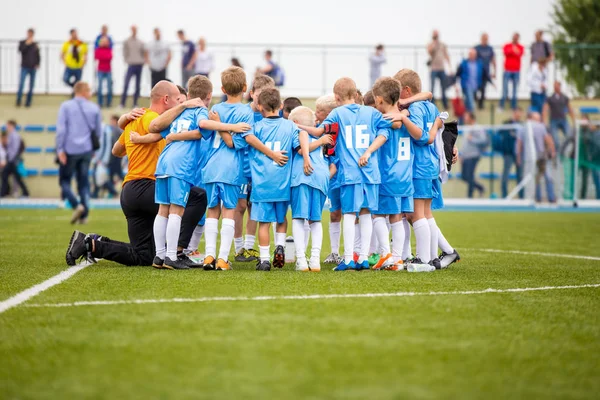 Equipe de futebol infantil com treinador. Um grupo de miúdos juntos no campo. Treinador dando instruções da equipe de futebol infantil. Conversa de grupo. Treinando a equipe de futebol juvenil antes do jogo — Fotografia de Stock