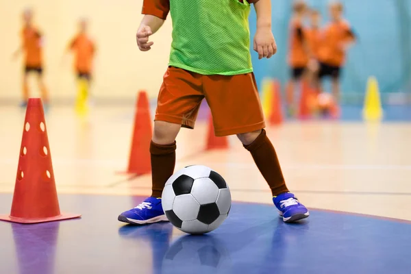 Футбольный мини-футбол для детей. Футбольная тренировка дриблинг конус дрель. Молодой футболист в помещении с футбольным мячом в спортзале. Игрок в оранжевой форме. Спортивный фон . — стоковое фото