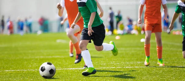 実行しているサッカー選手。サッカーの試合を蹴るサッカー選手若いサッカー選手がボールを実行しています。緑とオレンジ色のジャージー シャツ サッカー ボールを蹴るサッカー選手 — ストック写真
