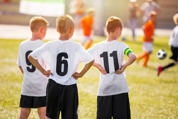 Kinderen van voetballers Team permanent op gras worp op een zonnige dag. Jonge jongens kijken naar voetbalwedstrijd. Jeugd voetballers van voetbal Academie. — Stockfoto