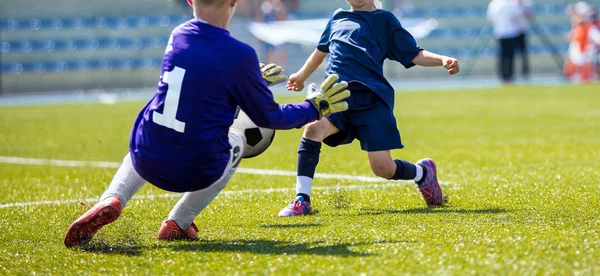 Young soccer goalkeeper save. Boy catching soccer ball. Football bench and children team in the background. Football match for children — Stock Photo, Image