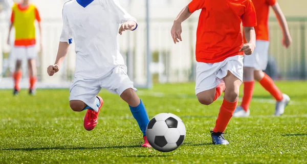 若いサッカー選手を実行します。フットボールを蹴る選手とのマッチゲームします。少年サッカーの選手がボールの後を実行しています。バック グラウンドでサッカー スタジアム。ピッチ上の少年がサッカーの試合 — ストック写真