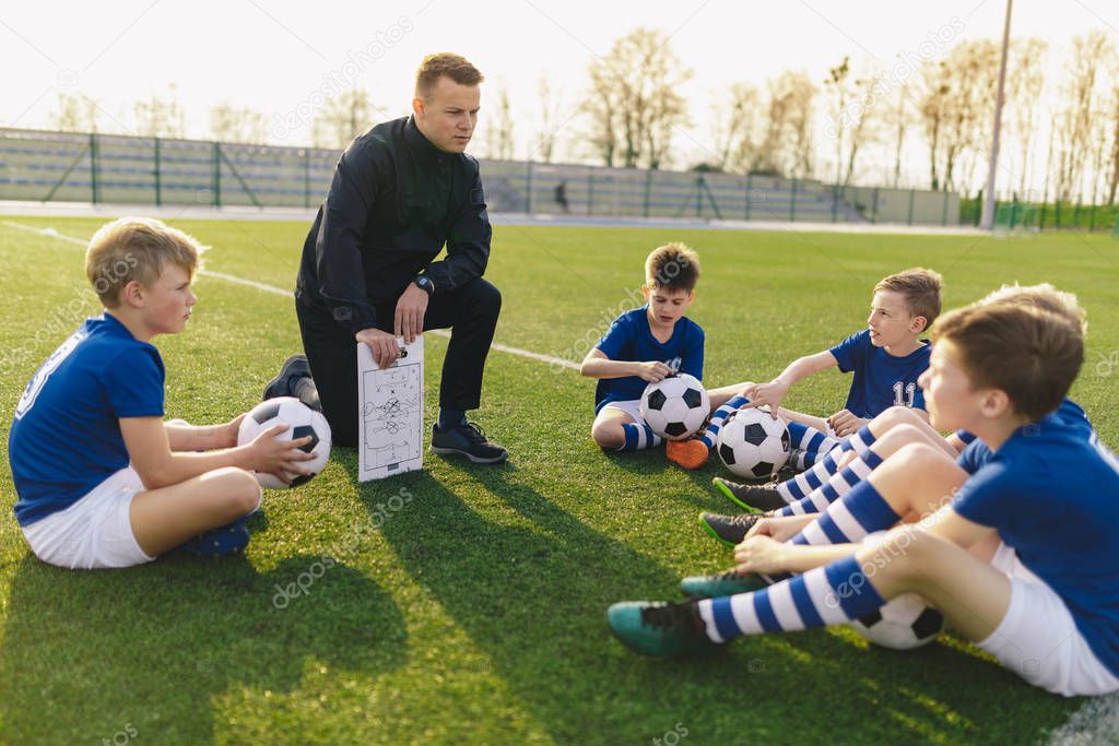 Group of Young Boys Sitting on Sports Grass Field witch School Coach. Kids Listening Coach's Tactic Talk. Young Coach Explain Football Tactic. Coaching Youths in Sports